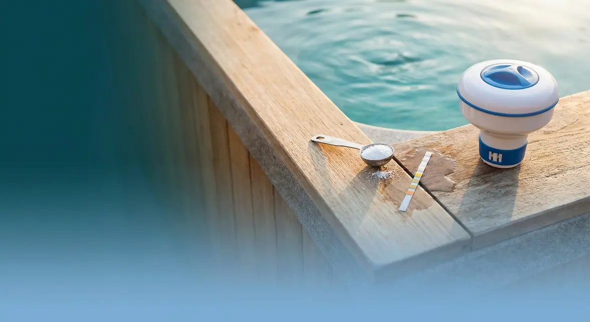 How to use chlorine in a hot tub — measuring spoon with granules and test strip on tub ledge